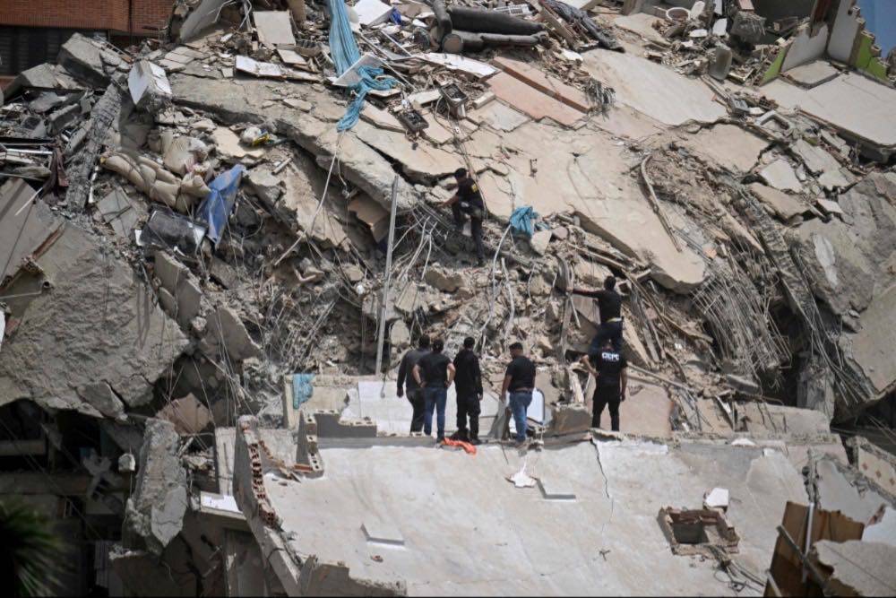 Rescue workers stand on the slab of a collapsed building amid twisted rebar and debris during search operations following an earthquake in Catia La Mar, La Guaira state, about 30 km northwest of Caracas. Photo by AFP