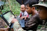 This photo taken on June 9, 2026 shows Chea Sareach (C), Biodiversity and Science Senior Coordinator of Conservation International Cambodia, ranger Hou Sophoan (R) and local community member Pan Sok (L) reviewing photos from a camera trap in the Cardamom mountain area in Koh Kong province. Above the patter of rain cascading through the jungle canopy comes the haunting call of a pileated gibbon singing to fend off intruders in Cambodia's Cardamom Mountains. - (Photo by TANG CHHIN SOTHY / AFP)