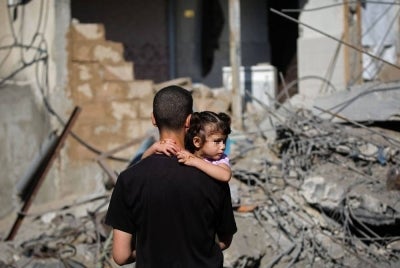 A displaced Palestinian man carries a girl while standing amid the debris of a building that was destroyed by an Israeli strike at Nuseirat refugee camp, in the central Gaza Strip on May 23, 2026. AFP photo.