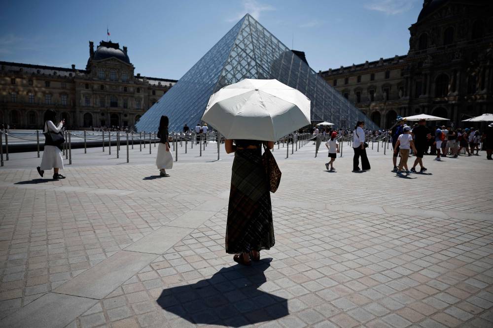 A person protects from the sun under an umbrella in front of the Louvre museum in Paris as a record-breaking early heatwave scorches a swathe of western Europe in May 2026. (Photo by AFP)
