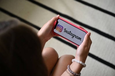 A teenager holds her smartphone displaying the logo of US social network Instagram (Photo by Nicolas TUCAT / AFP)
