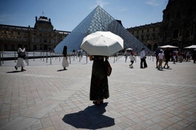 A person protects from the sun under an umbrella in front of the Louvre museum in Paris as a record-breaking early heatwave scorches a swathe of western Europe in May 2026. (Photo by AFP)