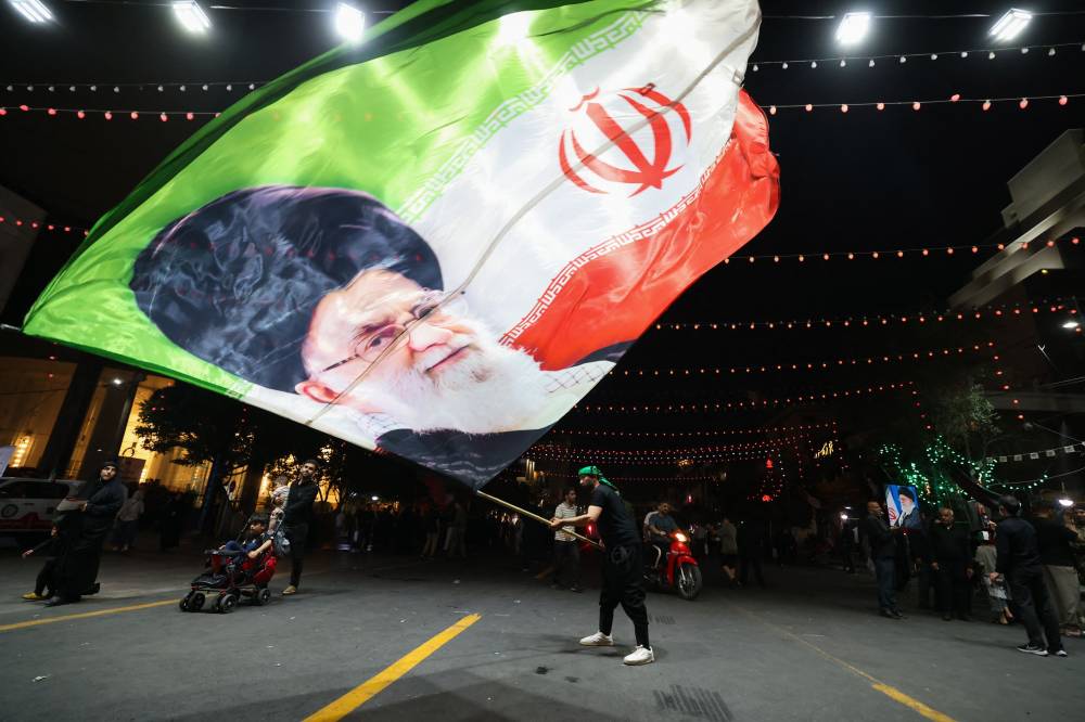 A man waves a flag near Imam Reza's shrine as mourners arrive for the funeral of slain Iranian leader Ali Khamenei and members of his family in Mashhad early on July 9, 2026. - (Photo by ATTA KENARE / AFP)