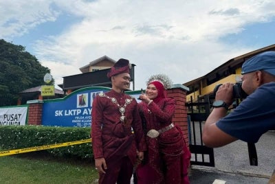 Nurul Aida, accompanied by groom Raja Akmal, shows her finger marked with indelible ink after casting her vote.