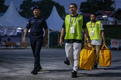 Election Commission (EC) officials, accompanied by police personnel, transport ballot boxes to the polling station for the N47 Kempas state constituency at Sekolah Kebangsaan Seri Melati during the 16th Johor State Election on July 11, 2026. (BERNAMA PHOTO)