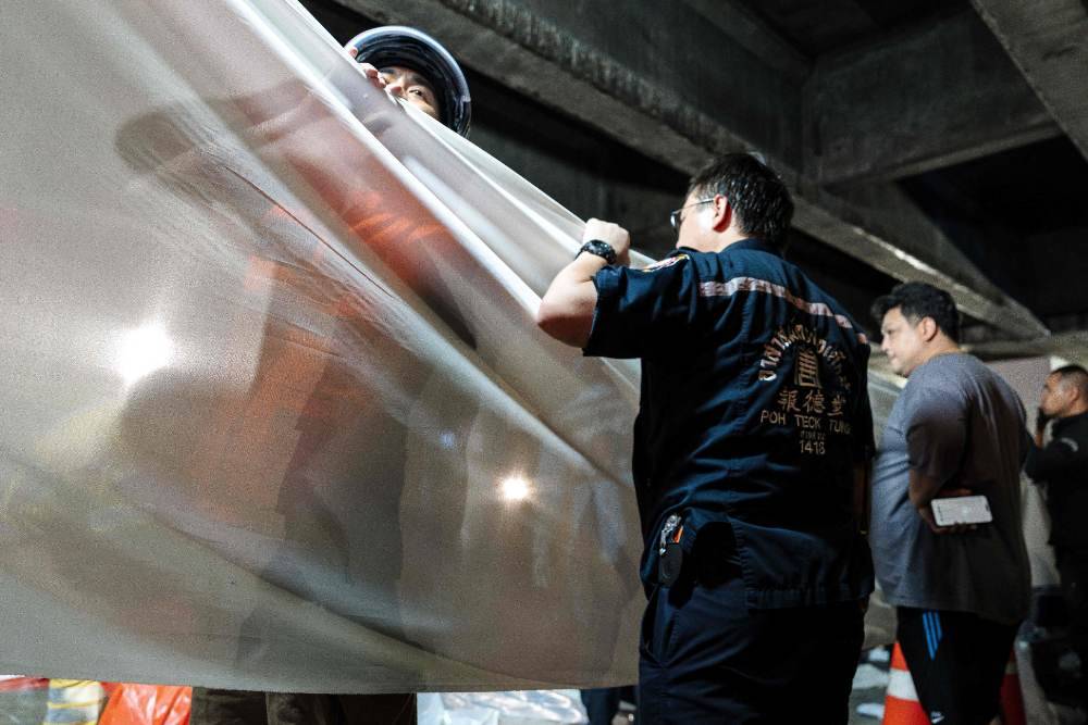 Emergency workers stand next to a white fabric displayed at the scene after a massive fire engulfed a bar in Bangkok. Photo by Chanakarn Loasarakham/AFP
