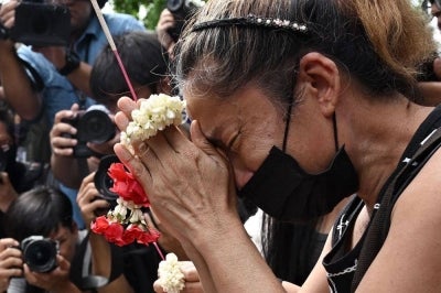 A woman, identified as Nid, prays for her deceased daughter Namtip Tubsook and her son-in-law Suwitcha Sirililung in front of the Rong Beer Na Lat Phrao bar in Bangkok on July 14. Photo by Lillian Suwanrumpha/AFP