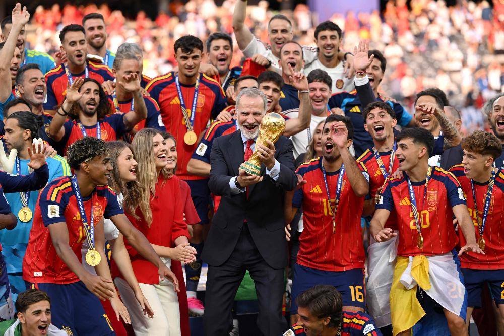 King Felipe VI of Spain lifts the FIFA World Cup Winner's Trophy while Queen Letizia of Spain, Princess Leonor of Spain and Princess Sofia of Spain and players of Spain watch at the award ceremony following the FIFA World Cup 2026 Final match between Spain and Argentina at New York New Jersey Stadium. Photo by AFP