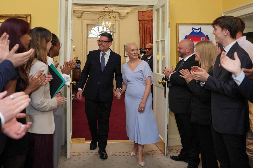 Staff appalud as Britain's new Prime Minister Andy Burnham and his wife Marie-France van Heel walk into 10 Downing Street in central London. Photo by Kin Cheung/AFP