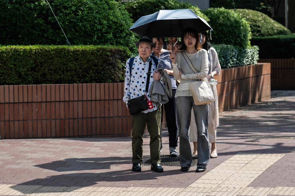 A group of women take shelter from the sun under umbrellas while waiting to cross a street in Tokyo on July 22, 2026 (Photo by Andrew CABALLERO-REYNOLDS / AFP)