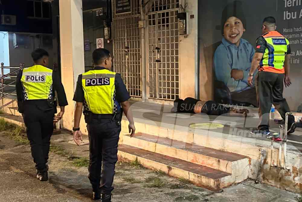 Authorities approach a man sleeping on the pavement outside a bank in Kota Bharu.