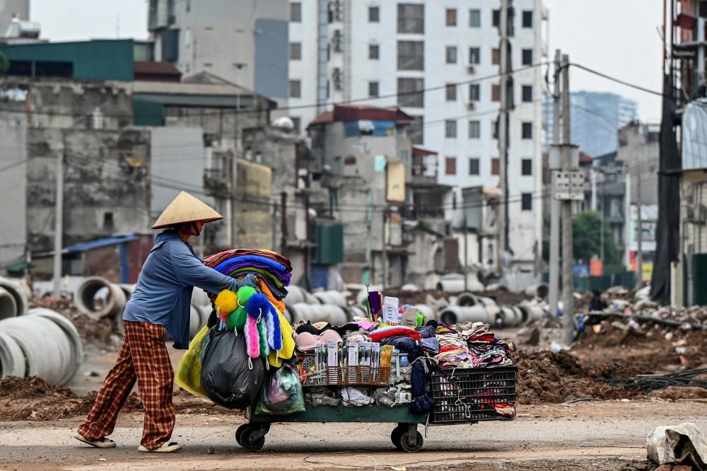 A woman pushes a cart past a road construction site in Hanoi on August 4, 2026. (Photo by Nhac NGUYEN / AFP)