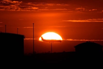 This picture taken on August 6, 2026, shows a passenger aircraft silhouetted against the setting sun on its approach to Sydney International Airport in Sydney. Dozens of commercial flights were delayed on August 7, at Sydney Airport as air traffic controllers used measures to prevent congestion, Airservices Australia said. No significant delays have occurred since midday, it added. (Photo by Saeed KHAN / AFP)