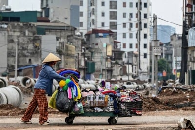 A woman pushes a cart past a road construction site in Hanoi on August 4, 2026. (Photo by Nhac NGUYEN / AFP)