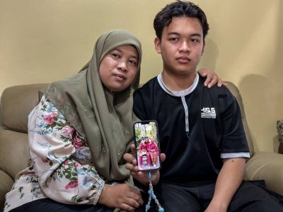 The wife of organ donor, Nor Asmani Ahmad, 44, and her only son, Muhammad Harith Mirza, 17, show a photograph of themselves with the late Mohd Khairil Jamaludin when met in Alor Setar, today. - Photo by Bernama