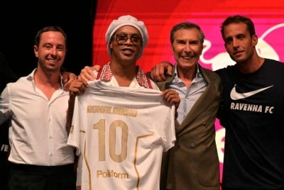 Newly recruited Brazilian football player Ronaldinho poses on stage with the jersey of Ravenna FC next to the president of the club, Ignazio Cipriani (R) during the team presentation in Marina di Ravenna on August 20, 2026. Former Ballon d'Or and World Cup winner Ronaldinho is set to come out of retirement aged 46 to play for Ravenna in the Italian third tier. - (Photo by Stefano RELLANDINI / AFP)