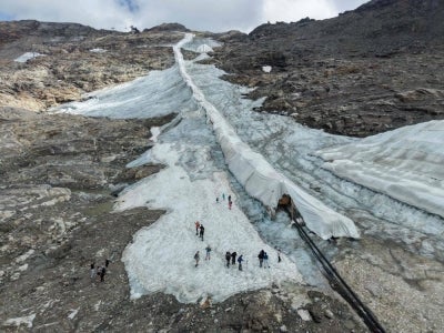 People walk beside protective fleece covering part of the Moelltal Glacier in Carinthia, Austria, on August 19, 2026, as the glacier has shrunk to a narrow strip of snow amid accelerating ice loss across the Alps, where glacier surface area has fallen 39 percent since 2000. (Photo by FRANZ NEUMAYR / AFP)