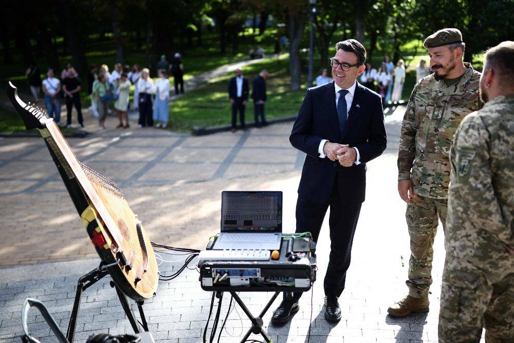 Britain's Prime Minister Andy Burnham (L), flanked by the head of the military and artistic unit who perform on the front lines, in hospitals, and at rehabilitation centres Cultural Forces Serial, Mikolay Siega (R), looks at an electric bandura, in a park near Mykhailivska Square. Photo by AFP