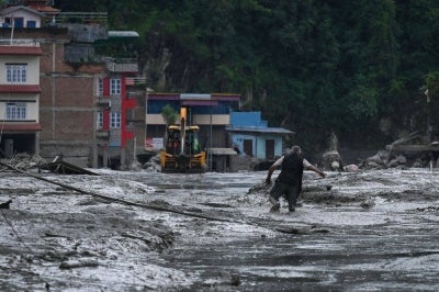 A resident walks along a street covered in mud following flash floods and a landslide disaster in Devghat, in Nepal's Nuwakot district. Photo by AFP