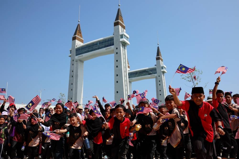 Students of Sekolah Kebangsaan (SK) Ladang wave the Jalur Gemilang against the backdrop of Terengganu’s iconic Kuala Terengganu Drawbridge in conjunction with the upcoming National Month celebrations. - Photo by Bernama