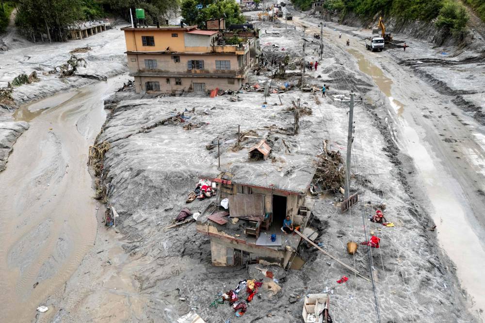 This aerial photograph shows Om Bahadur (front C), sitting on the ledge of his damaged house, a week after the devastating flash floods at Baireni in Nepal's Dhading district on Sept 2, 2026. - (Photo by MANAN VATSYAYANA / AFP)