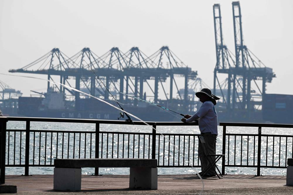 An angler fishes next to the container port terminal in Singapore on Sept 3, 2026. - (Photo by ROSLAN RAHMAN / AFP)
