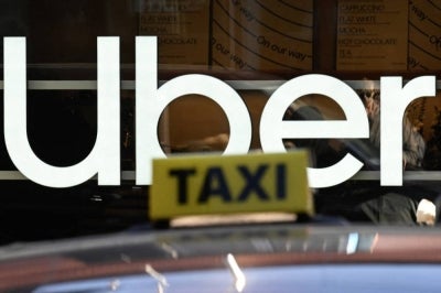 This photograph taken on Jan 20, 2026 shows A taxi logo atop a vehicle in front of illuminated Uber signage, on the sidelines of the World Economic Forum (WEF) annual meeting in Davos. - (Photo by INA FASSBENDER / AFP)
