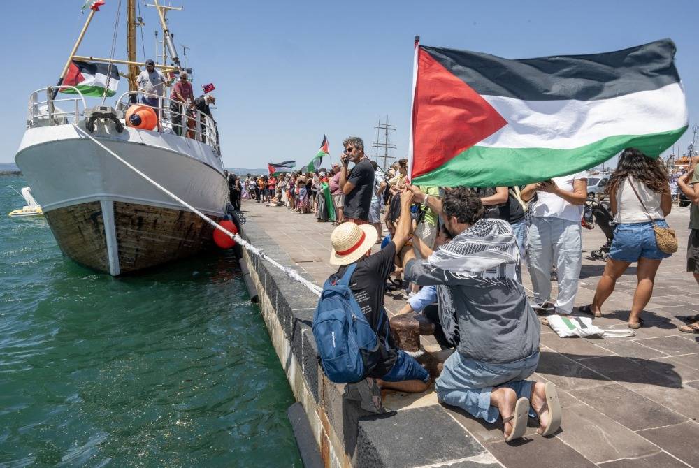 People gather with Palestinian flags around the Freedom Flotilla ship "Handala" ahead of the boat's departure for Gaza at a port in Syracuse, Sicily, southern Italy, on July 13, 2025. - (Photo by GIOVANNI ISOLINO / AFP)