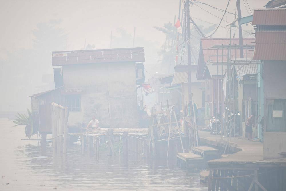 A man sits by the Kapuas river as thick smoke and haze shrouds the city of Pontianak in West Kalimantan on September 6, 2026. Indonesia has been battling for weeks to contain wildfires and thick smog, which has been drifting to Malaysia, Singapore and the Philippines. Photo by Bay Ismoyo/AFP