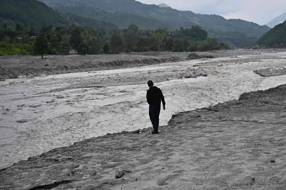 A man stands along a swollen river in the aftermath of flash floods at Devighat in Nepal's Nuwakot district on Sept 7, 2026. - (Photo by PEDRO PARDO / AFP)