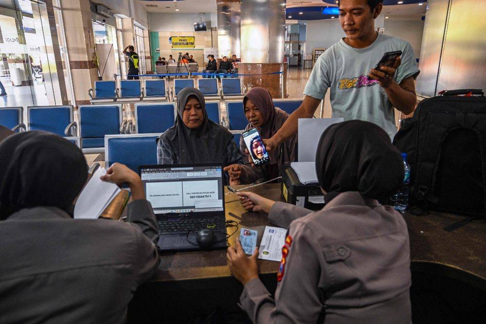 Police officers ask information from Ela Nur Atika (L), a wife of a passenger of the Virgo Transport 8, carrying 243 people, which met with an accident en route from Surabaya, East Java to Banjarmasin, South Kalimantan, as relatives seek information about loved ones at Tanjung Perak Port in Surabaya. Photo by AFP