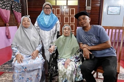 Senior citizen Saimah Sajiman (second, right), 102, affectionately known as 'Tok Saimah', with her daughter Fatimah Surip (left) and grandson Hairul Nizam (right) at her residence in Kampung Rahmat, Sri Lalang, Kluang. - Photo by Bernama