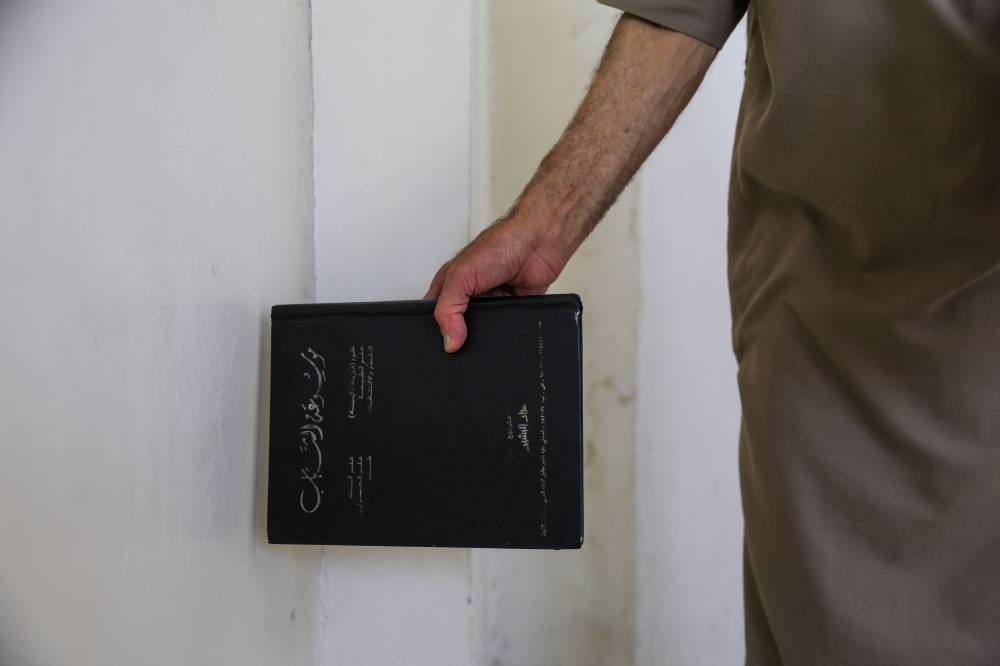 Mustafa Khaled Alwan, a 72-year-old Syrian man, holds a book next to what was a false wall where he hid his books for 15 years at the start of the uprising against longtime Syrian ruler Bashar al-Assad, in his home in the al-Bayadah neighbourhood in Homs on September 19, 2026. (Photo by Bakr ALKASEM / AFP)