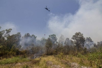 A helicopter drops water on burning forests and land in the Tegal Arum and Guntung Damar areas, Banjarbaru, in Indonesia’s South Kalimantan province on September 19, 2026. Toxic haze has shrouded parts of Indonesia, Malaysia and Singapore for weeks as Jakarta struggles to contain fires that have scorched large tracts of Borneo and Sumatra, with the smoke drifting across the region. (Photo by MUDA SAGALA / AFP)