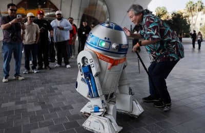 A visitor takes a photo with an R2-D2 droid during the sold-out opening day of the new Lucas Museum of Narrative Art, a 300,000 square foot structure in Exposition Park, on Sept 22, 2026 in Los Angeles, California. - (Photo by MARIO TAMA / Getty Images via AFP)