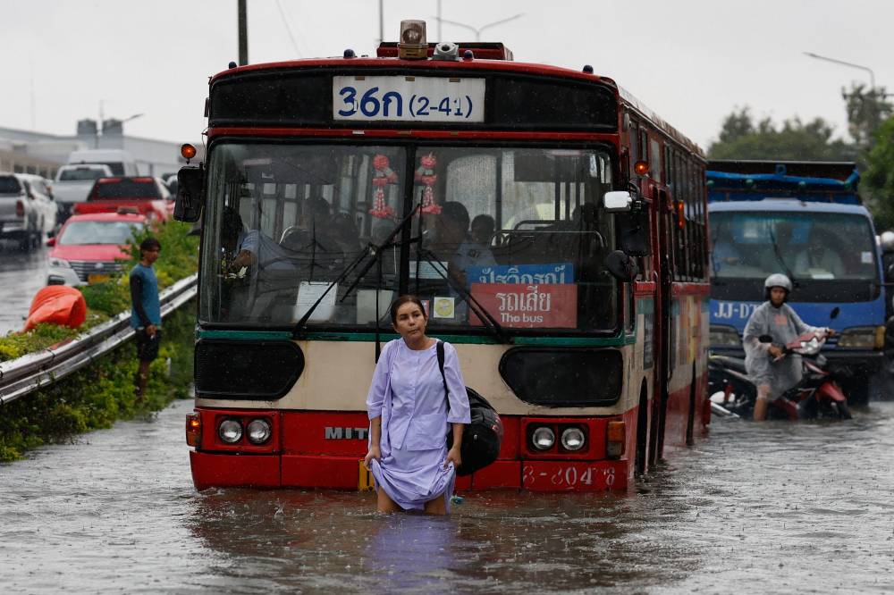 TOPSHOT - A woman walks through flood waters in front of a bus after heavy rain in Bangkok on September 26, 2026. Bangkok authorities declared a flood disaster across the Thai capital on September 26 after almost 48 hours of heavy rain left canals full, roads submerged and residents knee-deep in water. (Photo by Sarot Meksophawannakul / AFP)