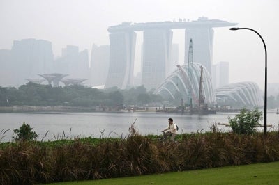 A cyclist rides along the Marina bay east garden as the city skyline is shrouded with haze in Singapore on September 28, 2026. Indonesia has been battling fires for weeks in parts of Borneo and Sumatra, sending suffocating haze across the islands and neighbouring Malaysia and Singapore. (Photo by Roslan RAHMAN / AFP)