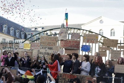 Protesters stand behind the gates of the Michelet high school, covered with placards, as confetti is thrown during a demonstration of high-school students as part of a nationwide protest movement over learning conditions in Vanves, outside Paris, on October 6, 2026. Since late September, pupils have barred the entrances to hundreds of schools, complaining of teacher absences, overloaded timetables, dilapidated classrooms and buildings ill-adapted to rising temperatures, among other grievances. (Photo by GEOFFROY VAN DER HASSELT / AFP)