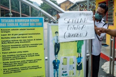 A security guard at SMK Dato’ Bentara Luar in Batu Pahat puts up a notice announcing the school’s closure due to haze. -Bernama Photo