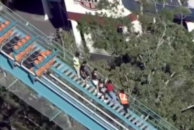 A screenshot from 11Alive’s broadcast shows the Goliath roller coaster at Six Flags Over Georgia stopped on the tracks as riders are helped to the ground following an incident that left one person dead and several others injured.