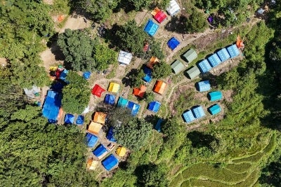 This photograph taken on October 1, 2026 shows an aerial view of temporary shelter tents uphill in Betrawati in Nepal's Nuwakot district in the aftermath of the August 26 flash flood. More than 1,400 people died and over 5,000 remain missing after tsunami-like waves swept through northern mountainous areas, destroying homes, roads, bridges and settlements. Government report shows that more than 7,500 private houses were damaged in the floods. (Photo by Prakash MATHEMA / AFP)