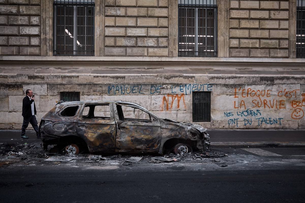 A man walks past a burnt out car on Rue Yves Toudic destroyed after a weekend of protests against the "high cost of living", in central Paris on October 19, 2026. France's Prime Minister said 1,200 people were arrested in protests across the country on October 17, and 150 police were hurt during clashes between police and protesters. Massive looting and multiple blazes gripped France as nationwide marches against soaring inflation degenerated into street violence of "extreme intensity". (Photo by Kiran RIDLEY / AFP)