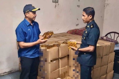 Kedah Domestic Trade and Cost of Living Ministry director Muhammad Nizam Jamaludin (left) inspects the subsidised packet cooking oil seized at the warehouse.