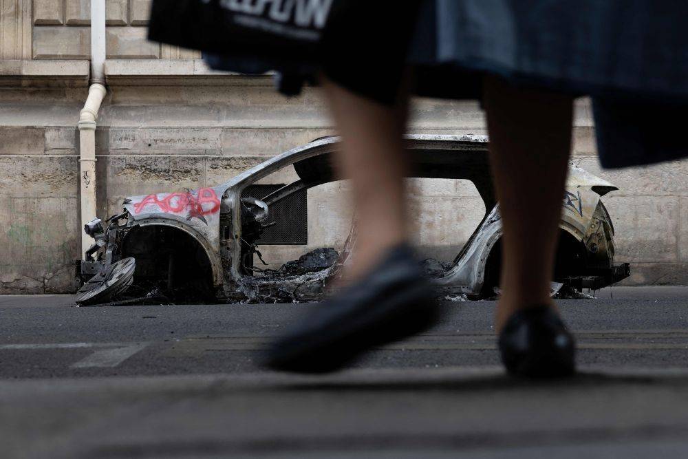 An elderly woman walks past the wreckage of a burnt-out car, spray-painted with "ACAB - All Cops Are Bastards" on a street in Paris on Oct 19. AFP FILE PIX