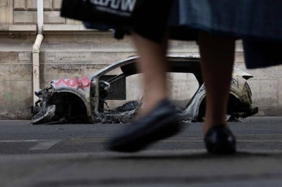 An elderly woman walks past the wreckage of a burnt-out car, spray-painted with "ACAB - All Cops Are Bastards" on a street in Paris on Oct 19. AFP FILE PIX