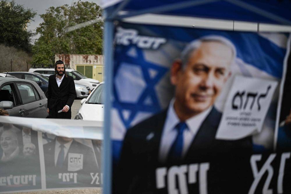 A voter walks past campaign posters of Prime Minister Benjamin Netanyahu as he arrives at a polling station in Jerusalem on Oct 27. Photo by AFP
