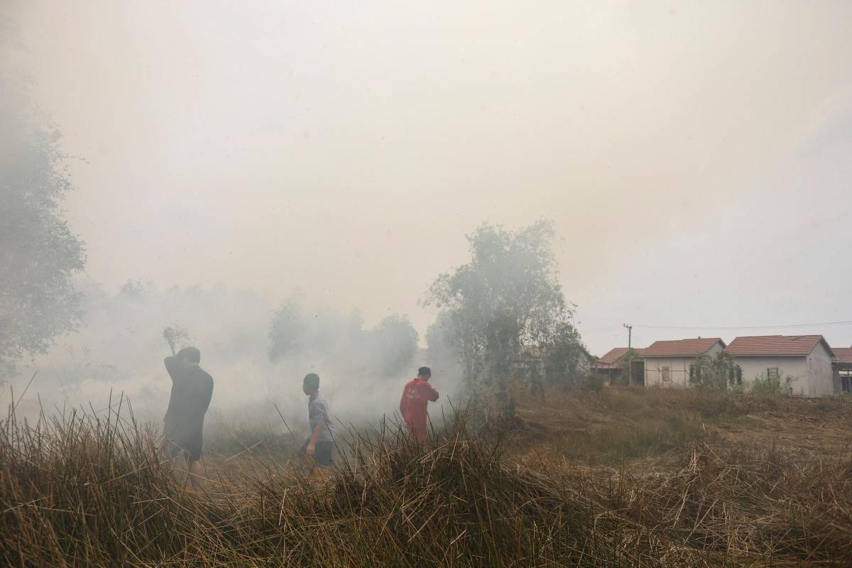 A child walks among volunteers struggling to extinguish a land fire that reignited behind an elementary school at Alalak village in Barito Kuala Regency, South Kalimantan on October 28, 2026.(Photo by MUDA SAGALA / AFP)