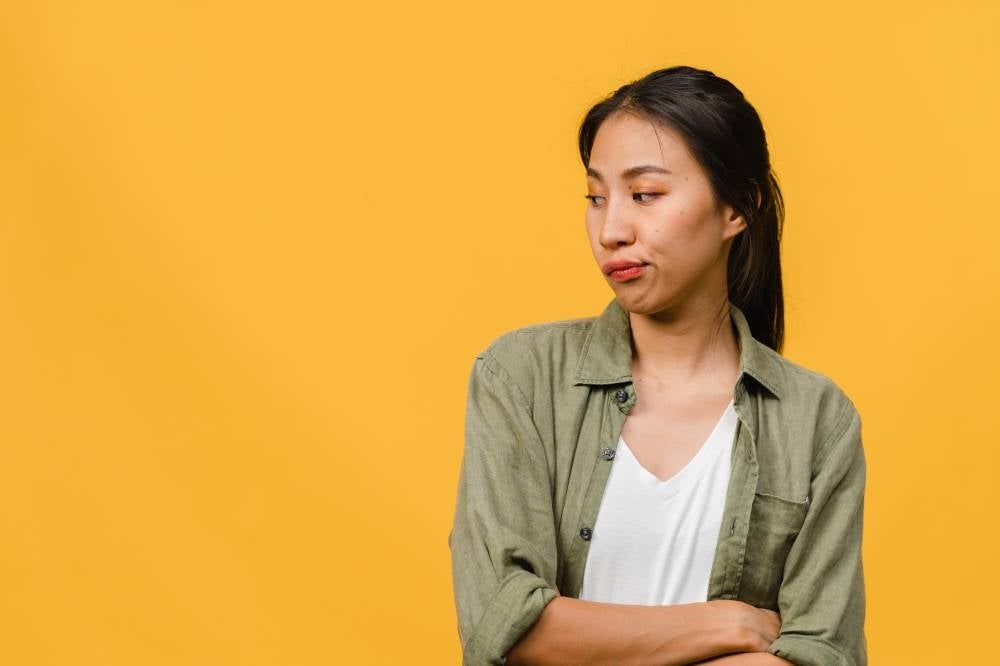 Portrait of young Asia lady with negative expression, excited screaming, crying emotional angry in casual clothing isolated on yellow background with blank copy space. Facial expression concept.