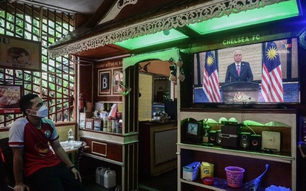 Seorang pekerja sebuah kedai makan menonton siaran langsung ucapan khas Perdana Menteri pada Ahad.