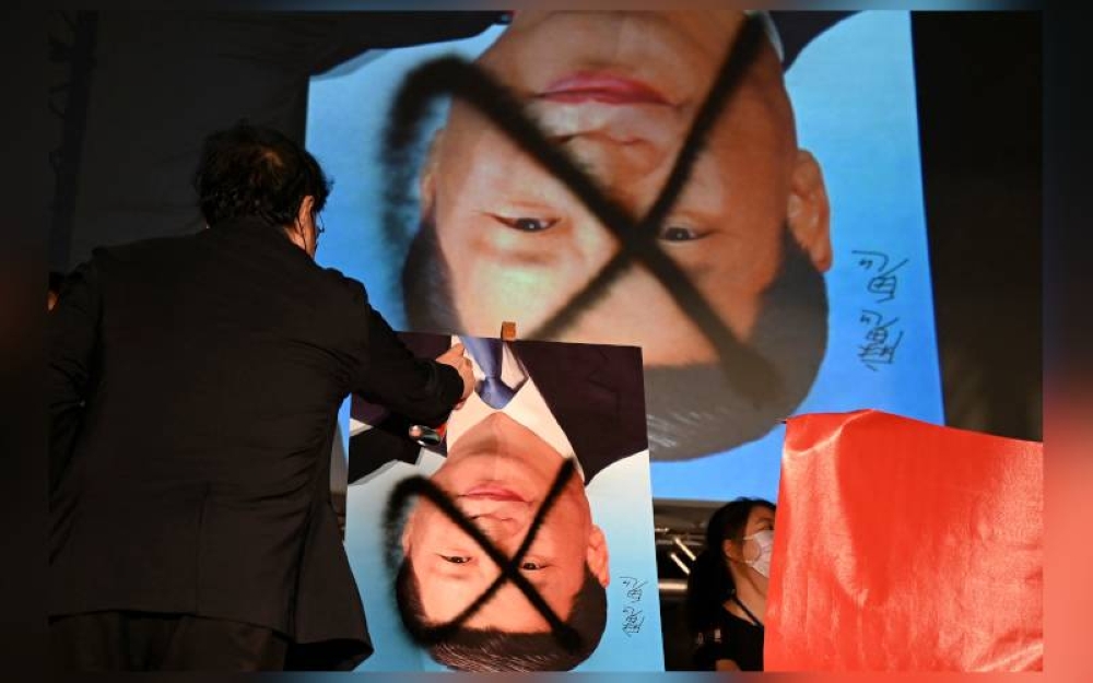 Seorang penunjuk perasaan menyembur poster Presiden China, Xi Jinping di luar Parlimen di Taipei. - AFP